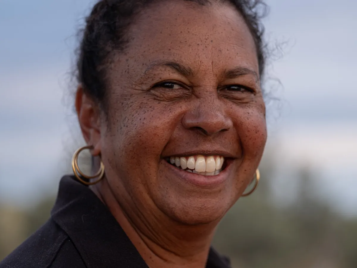 A smiling guide in a black polo shirt, photographed outdoors among native scrub.